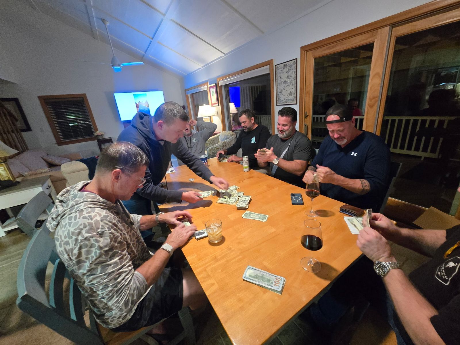 Players around the dining table at the beach house rolling dice for Qualifier, with cash on the table