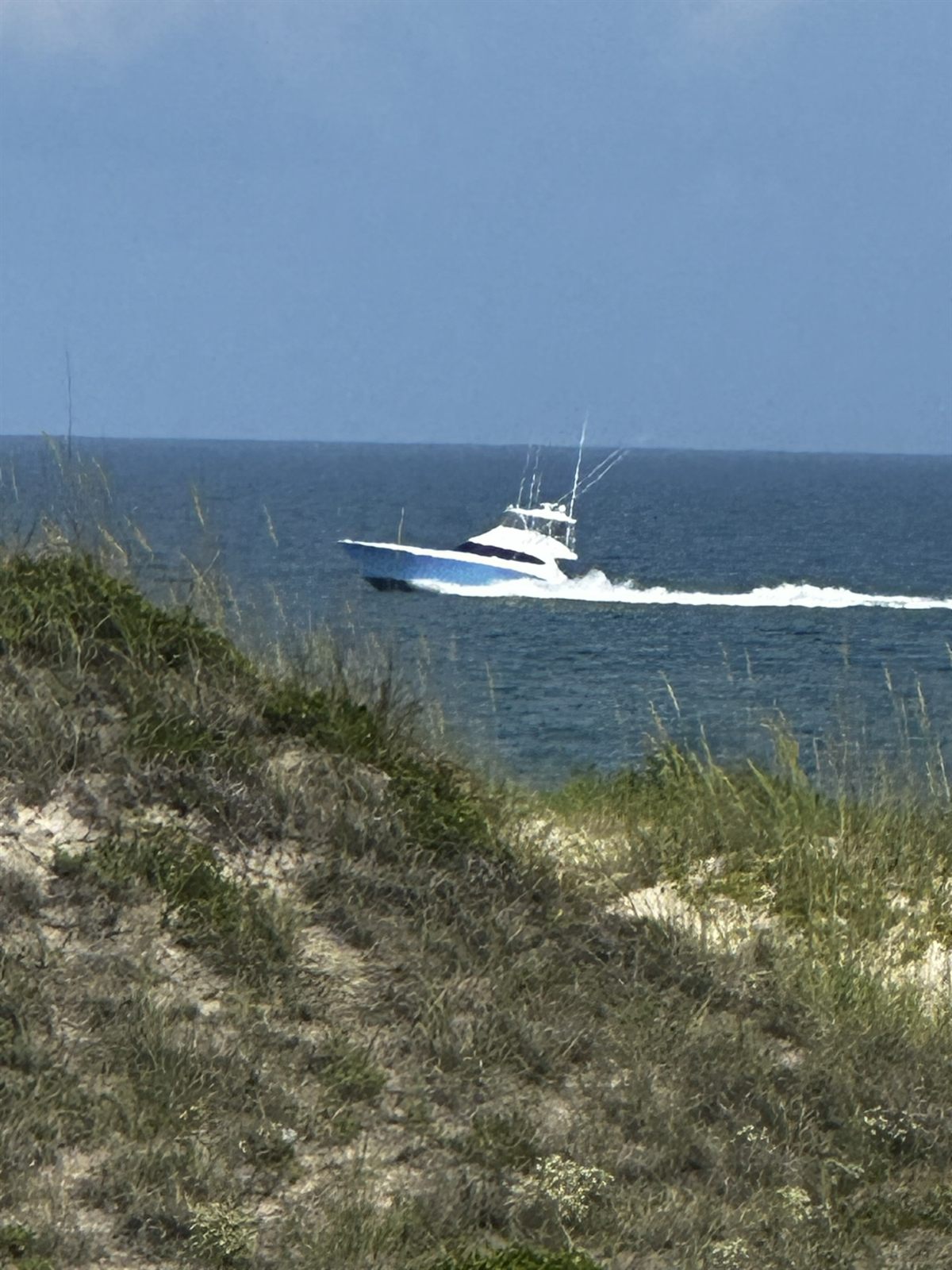 A sportfishing boat heading offshore past the dunes